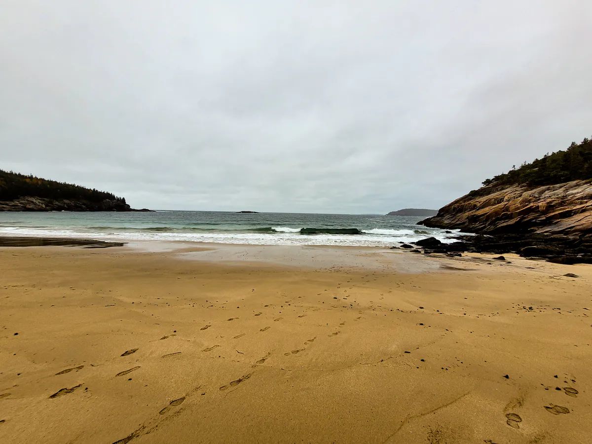 Sand Beach in Acadia National Park, a curve of pale sand inside a granite cove with cold Atlantic water and pine-covered cliffs