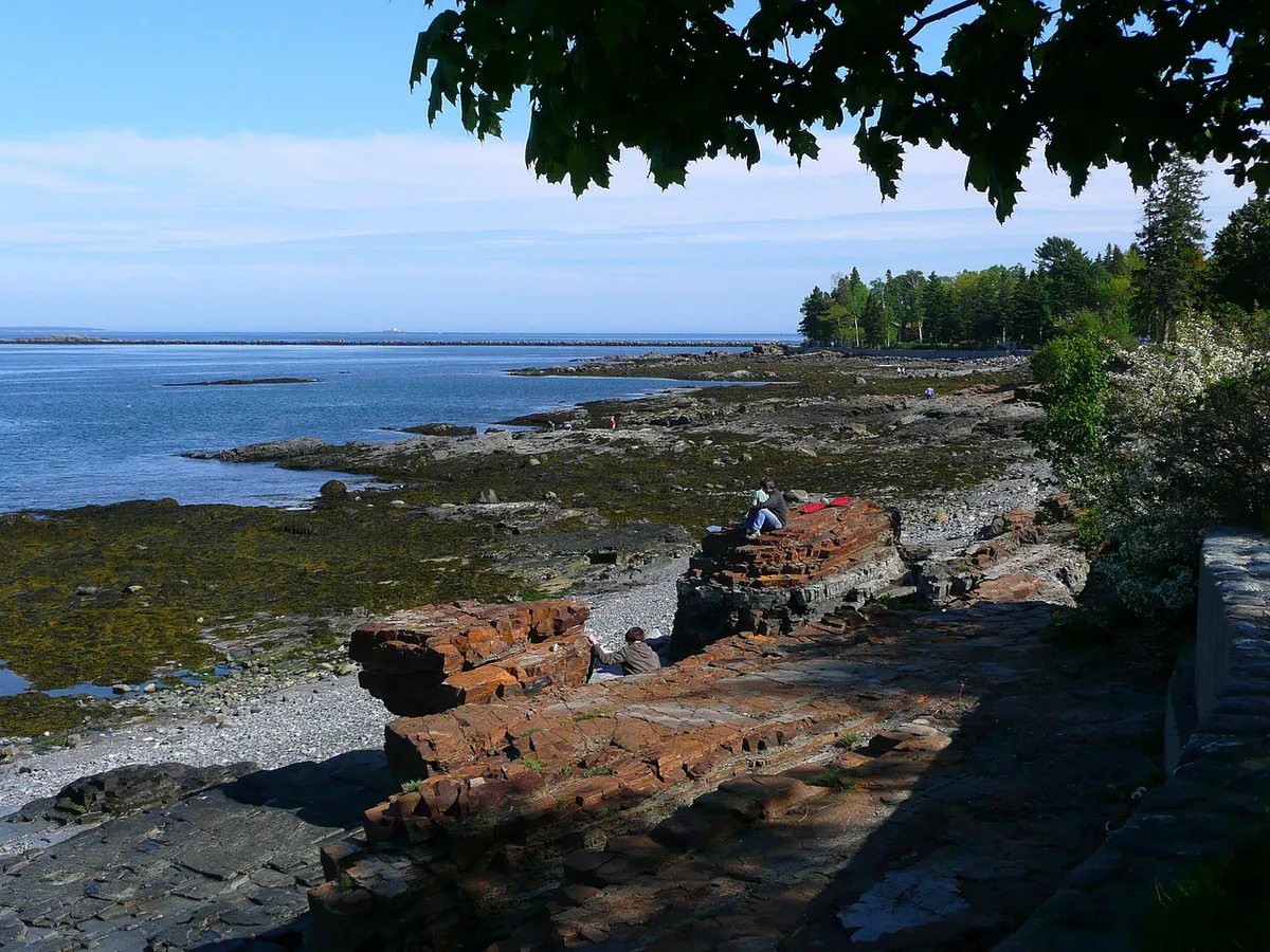 A rocky pink granite shoreline in Acadia National Park, with people exploring the tide zone