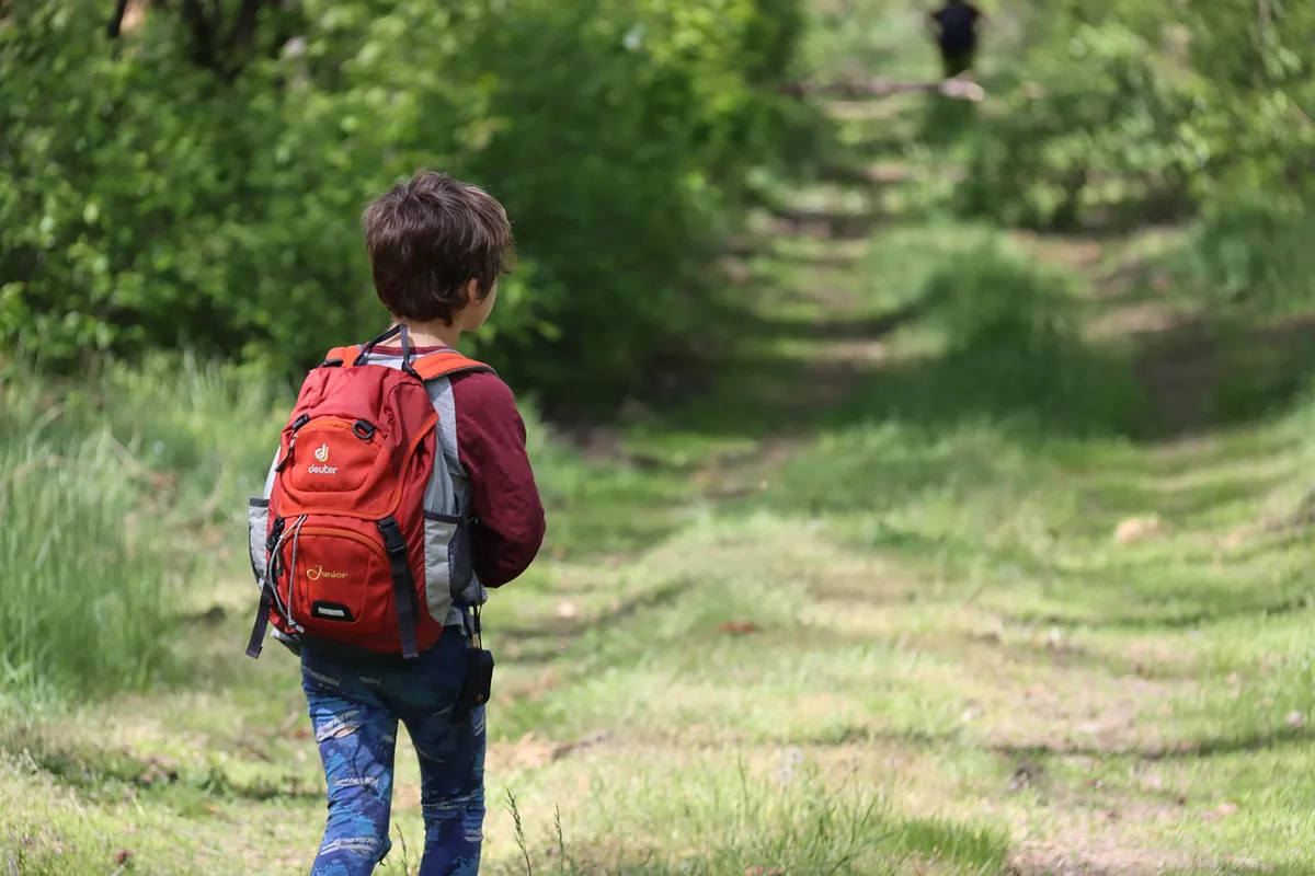 A young boy hiking a grassy forest trail wearing a Deuter daypack