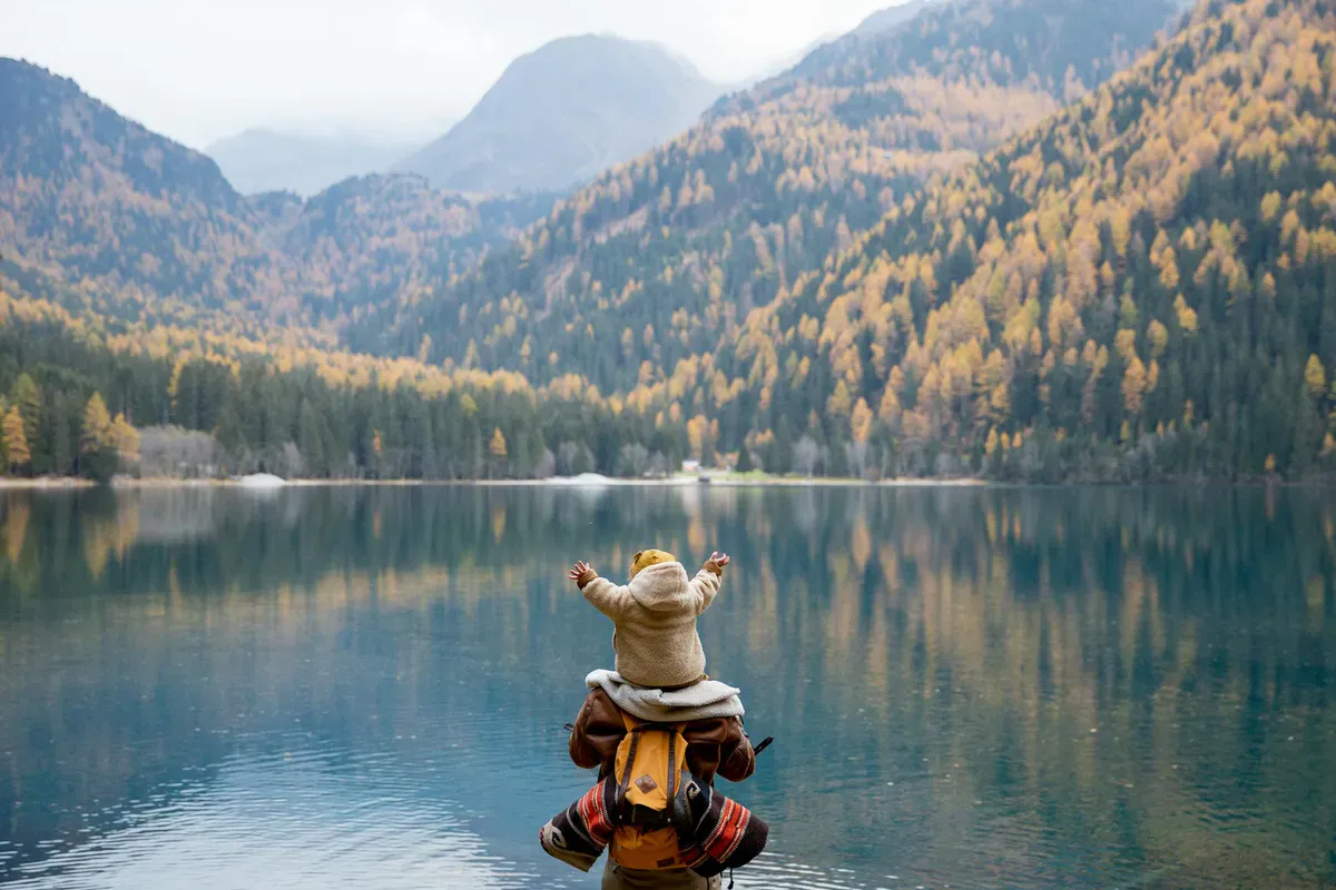 A parent and child sitting on a lakeside log overlooking a mountain view, the kind of payoff that makes a family hike memorable