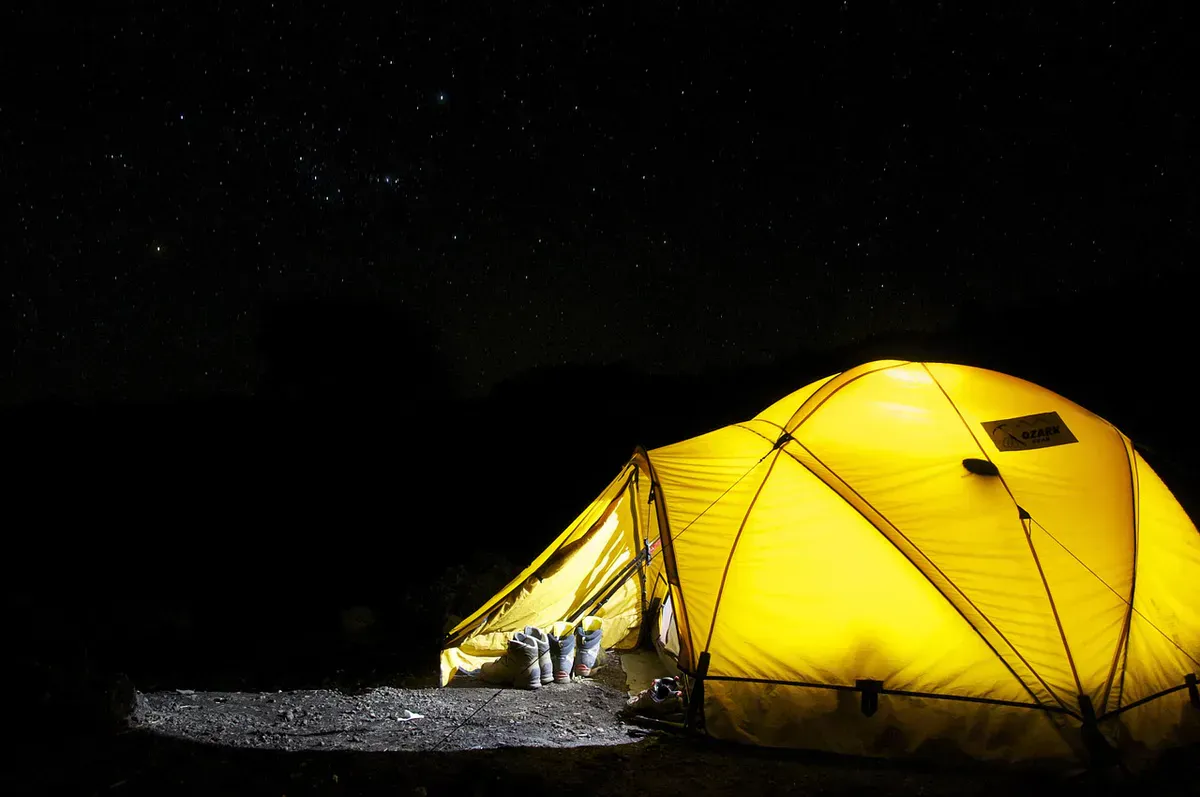 A yellow dome tent lit from within under a starry night sky, showing the kind of weather-tight shelter a Maine night demands